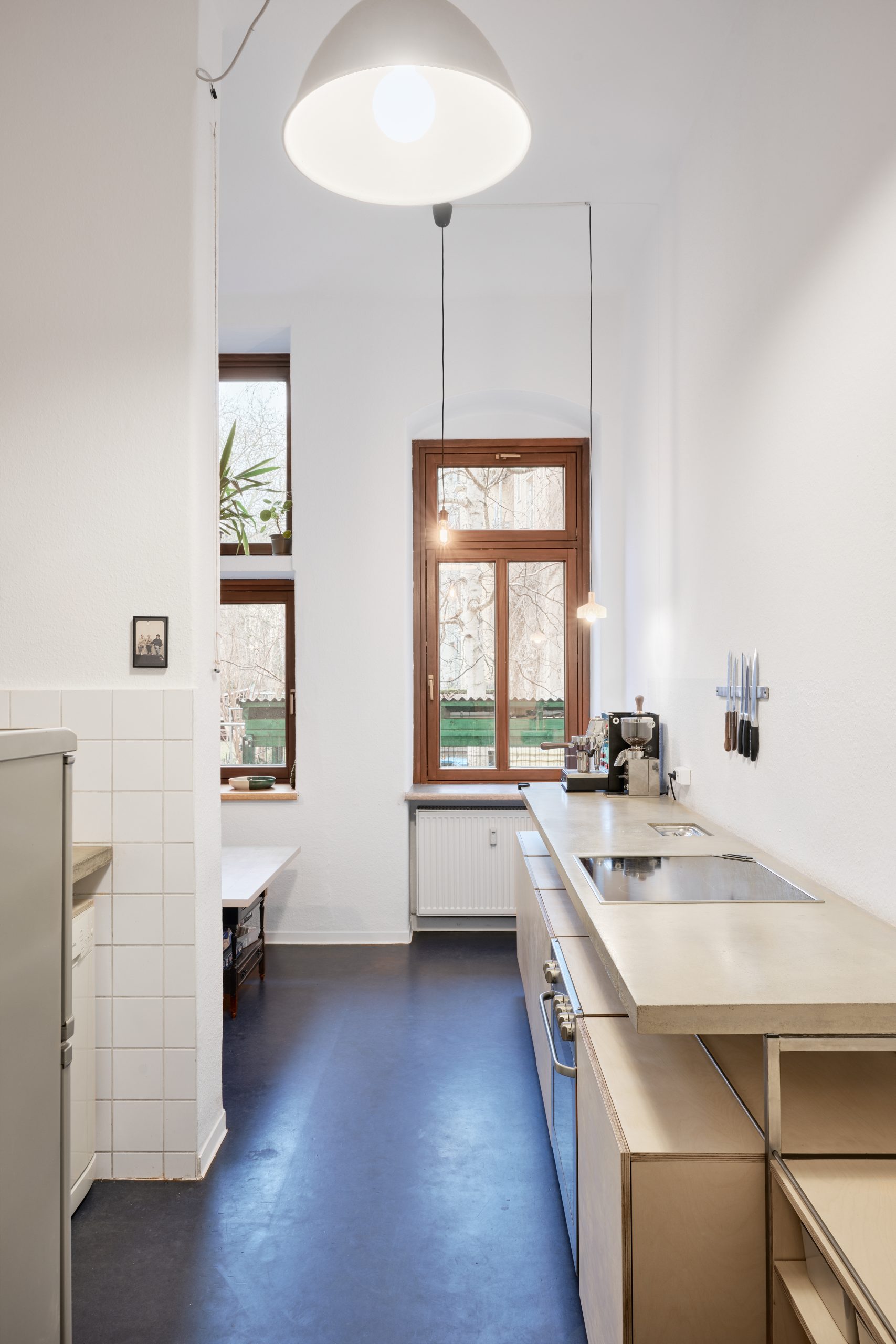 Blick durch die Küche mit Kühlschrank, Betonarbeitsplatten und offenen Regalen