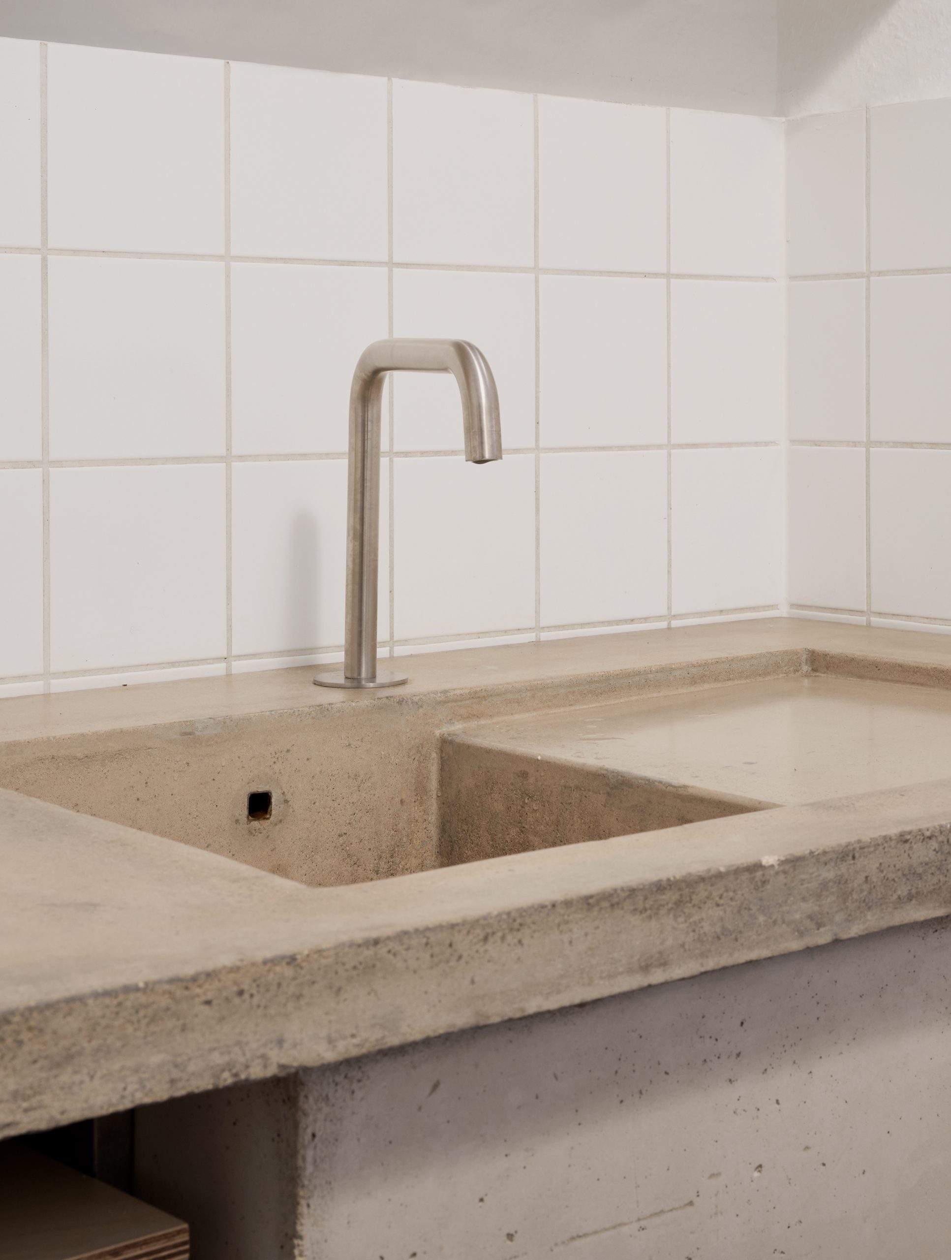 Gegossenes Betonbecken mit Edelstahlarmatur vor einer weiß gefliesten Wand