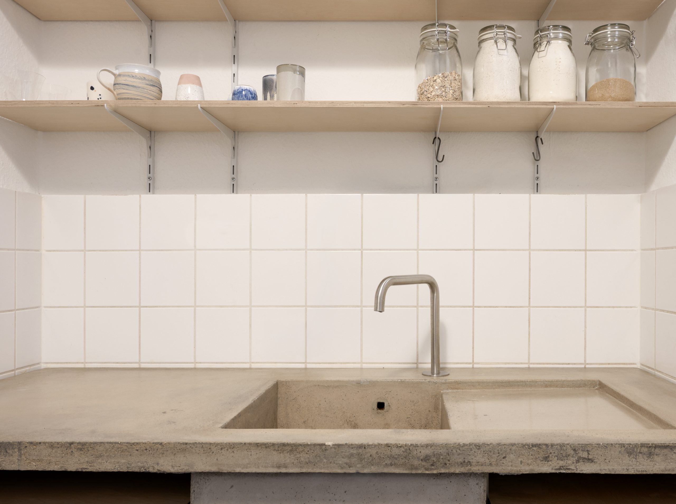 Breite Ansicht der Betonarbeitsfläche mit Becken, Armatur, Fliesenspiegel und offenen Regalen