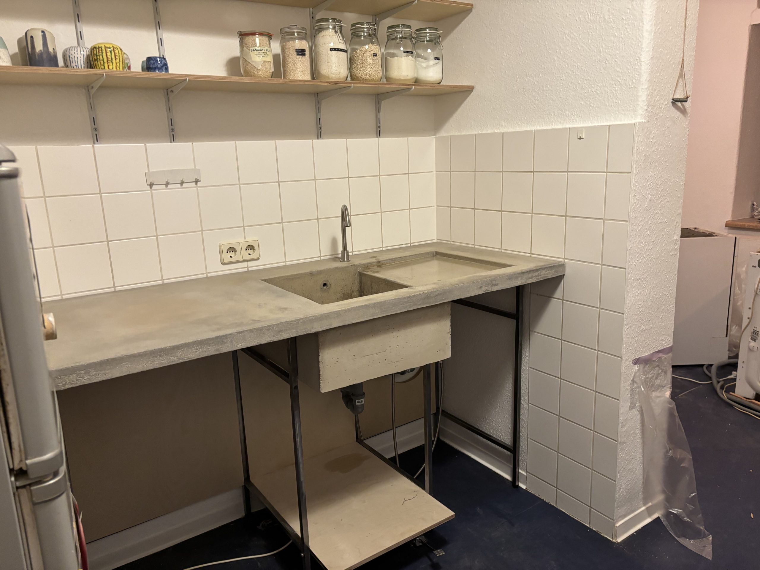 Weitgehend fertige Betonarbeitsfläche mit Becken, Stahlgestell und kleinem Fußpedal am Boden