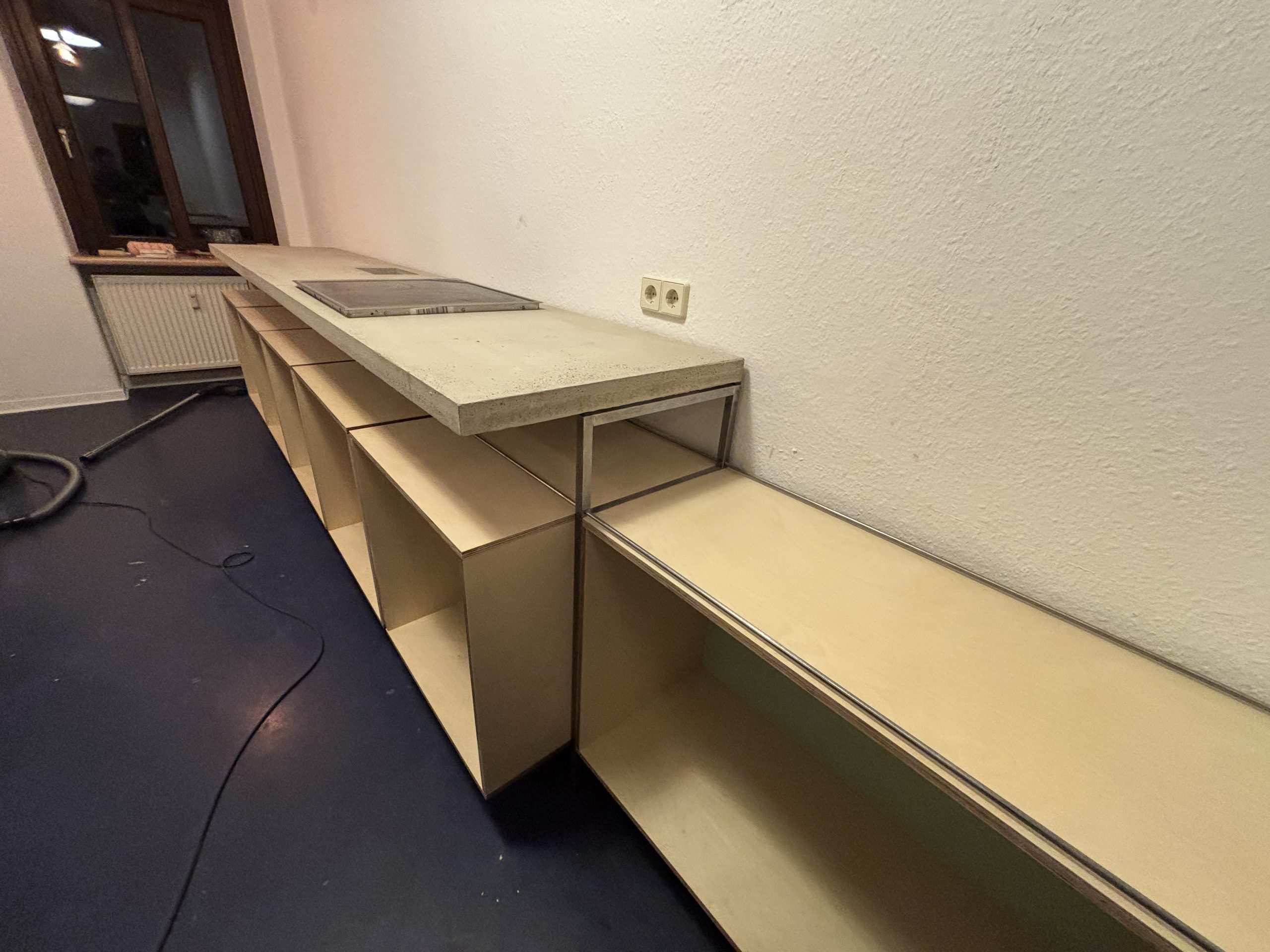 Lange Küchenzeile mit aufgelegter Betonplatte und eingesetztem Kochfeld während des Aufbaus