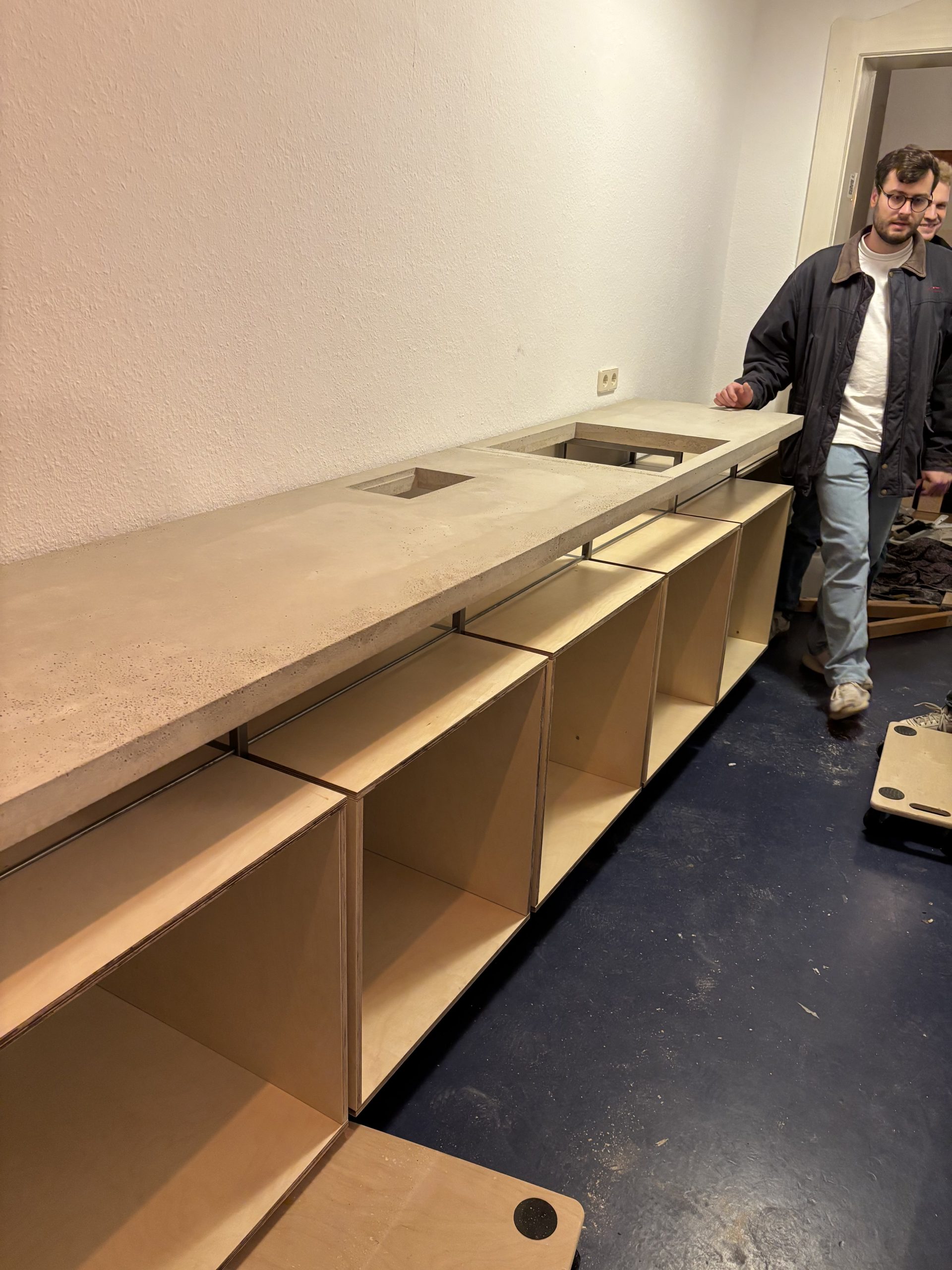 Betonarbeitsplatte mit Aussparungen für Kochfeld und Biomüll wird auf das Untergestell gelegt