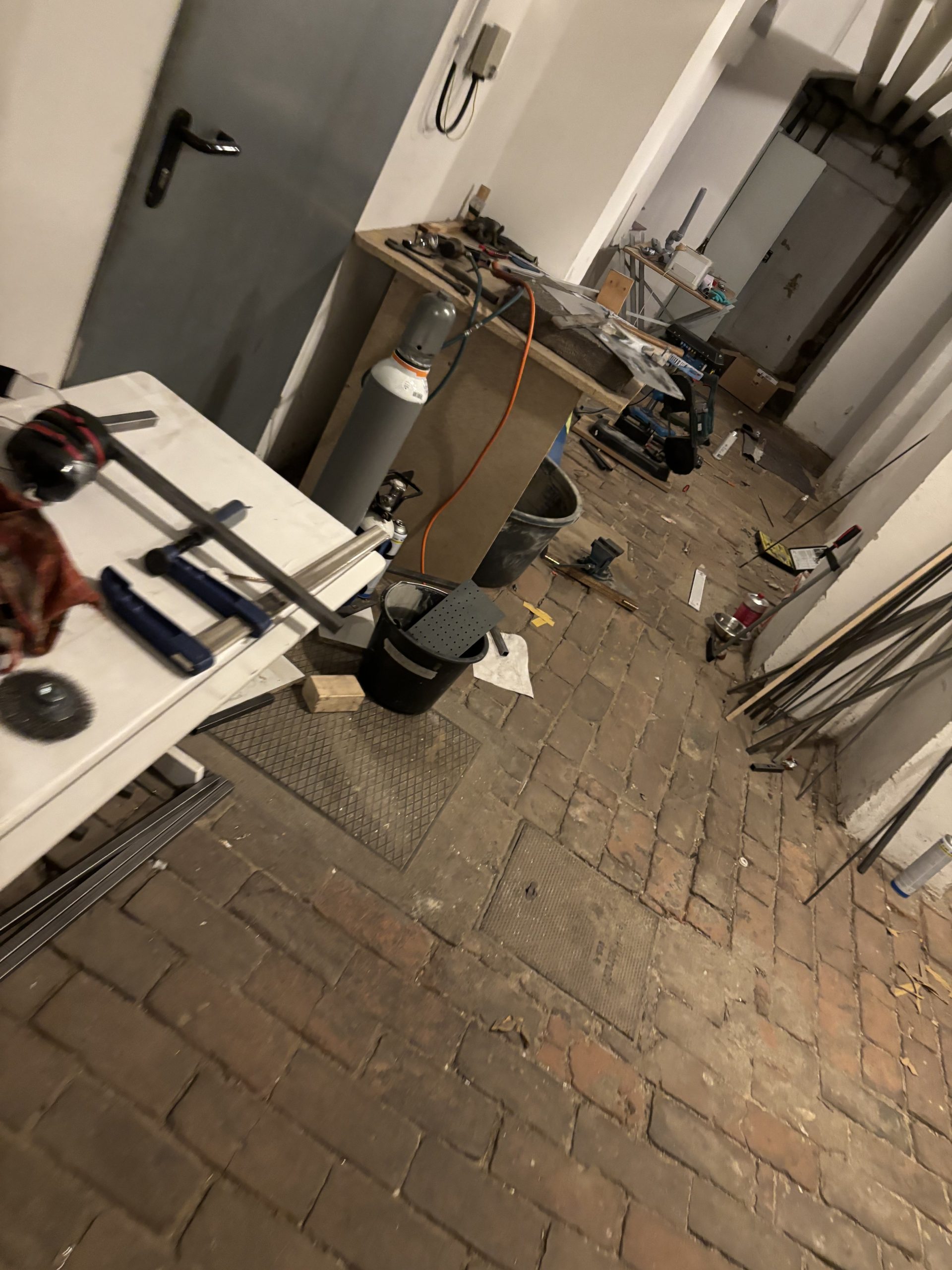 Provisorischer Arbeitsbereich mit Metallwerkzeugen, Gasflasche und Rohmaterial