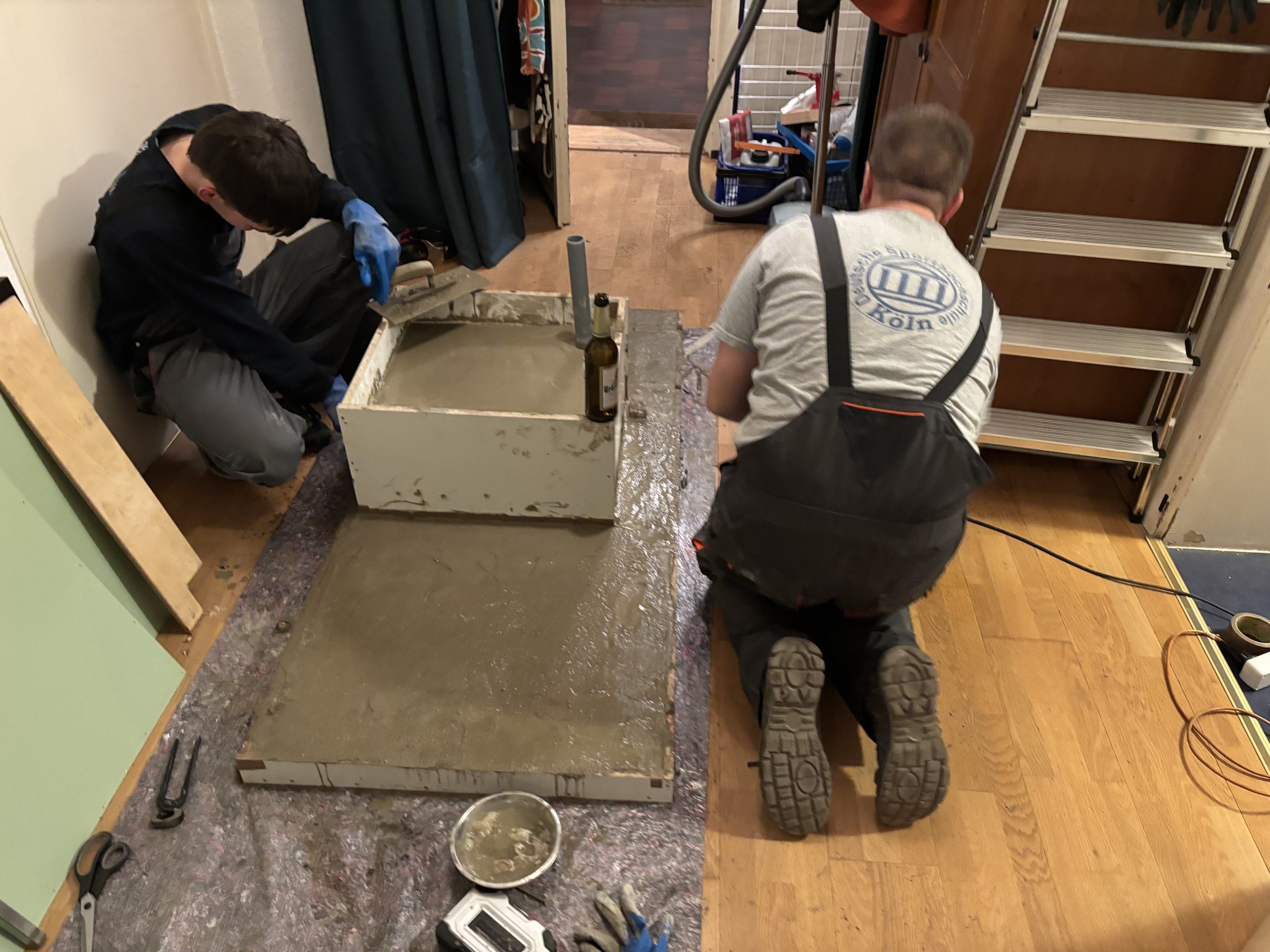 Zwei Personen glätten gemeinsam frischen Beton in einer selbst gebauten Schalung